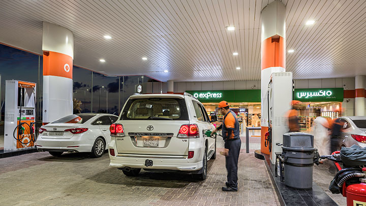 A woman fills her car’s tank at a gas station under the bright lights of Philips canopy lighting.